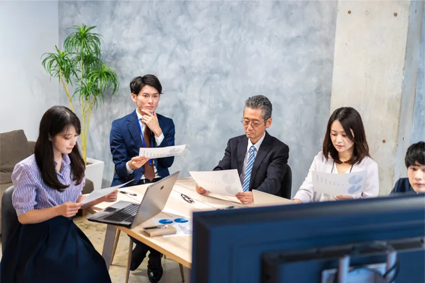 5人の社員が資料を見ながら会議をしている様子の写真
