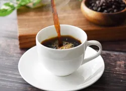 テーブルに置いた白いティーカップにコーヒーを注いでいる写真
