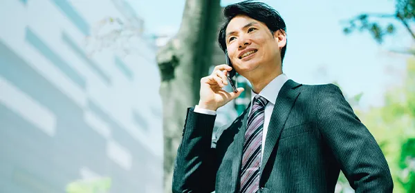 スマートフォンを耳に当てて話しながら歩くスーツ姿の男性の写真