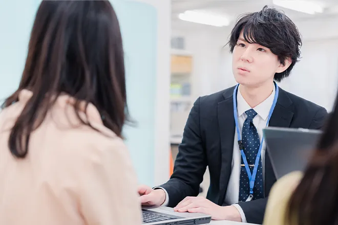ノートパソコンを操作しながら女性の話を真剣な面持ちで聞いている男性社員の写真